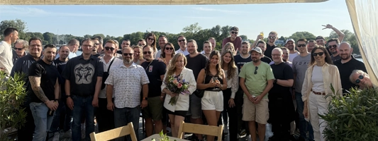 JAEMACOM Team bei einer Bootsfahrt auf der Berliner Spree, Kollegen stehen zusammen auf dem Deck mit der U-Bahn-Brücke im Hintergrund